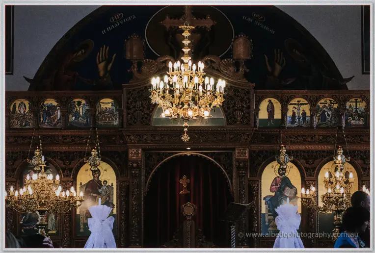 Glowing brass chandeliers hanging above the ornate carved iconostasis of the Orthodox church