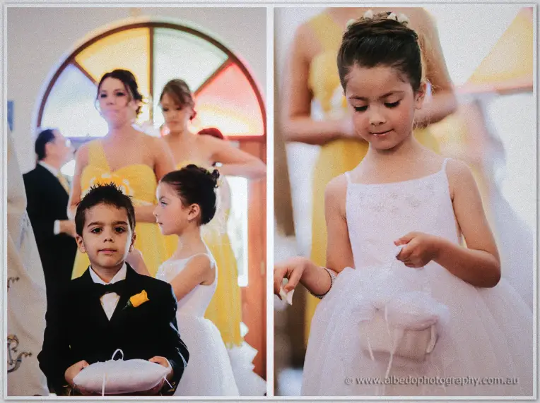 Ring bearer in a tiny tuxedo with his flower girl and yellow-clad bridesmaids by stained glass