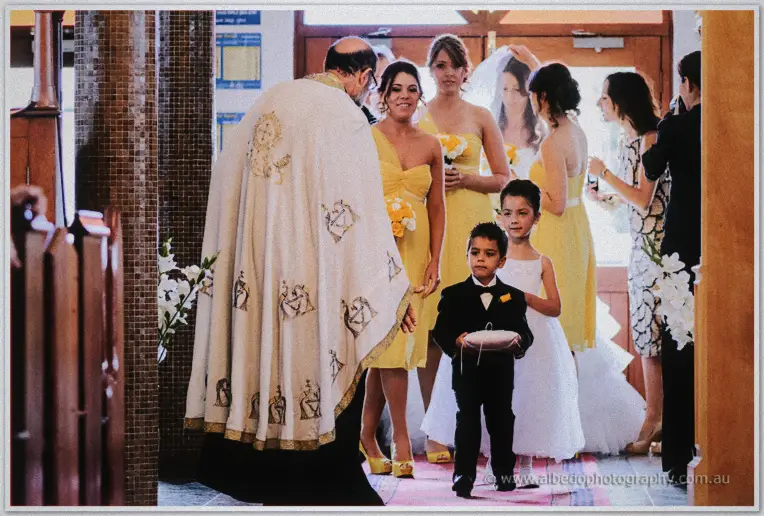 Priest greeting the bridal party as a small page boy carries the rings down the church aisle