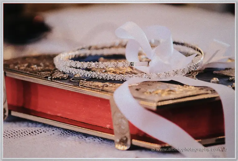 Jewelled wedding crowns tied with white ribbon resting on an ornate red and gold gospel book