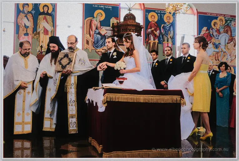 Priests blessing the couple at a small table while the bridal party gathers inside the icon-filled church