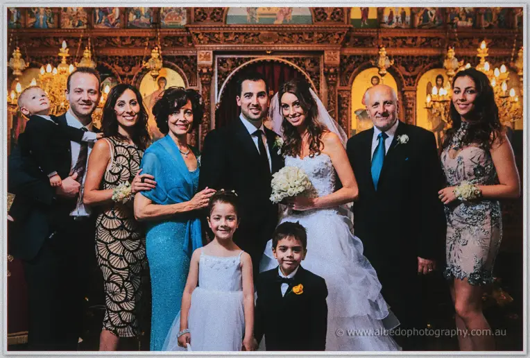 Family and friends gather around Michele and Nick for a group portrait inside the candlelit Orthodox church.