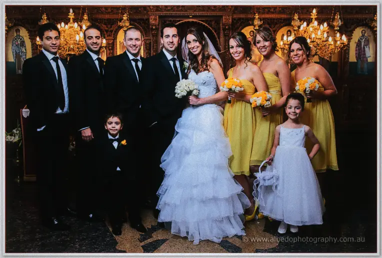 The full bridal party gathers in the church, yellow bridesmaid gowns bright against gilded icons.
