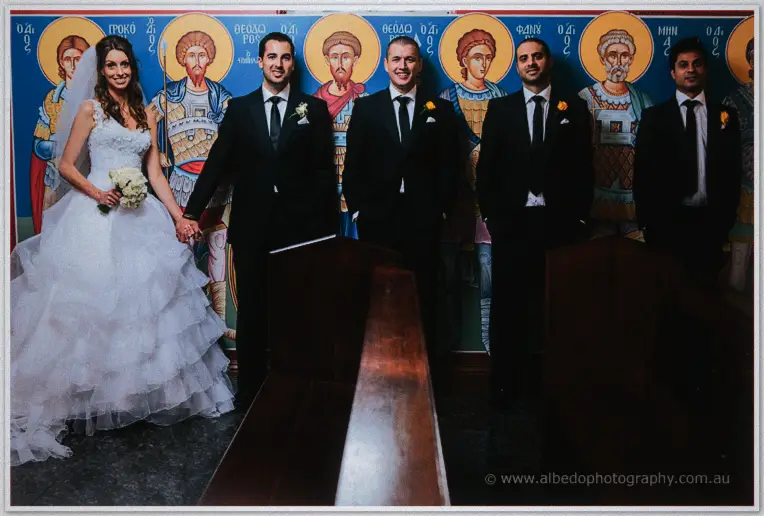 Groomsmen in black suits share a laugh with the newlyweds in front of the church's painted saints.