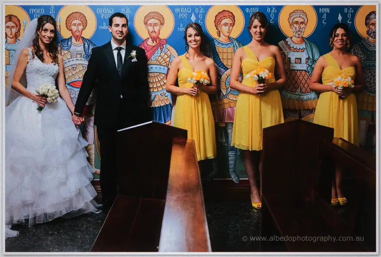 Bridesmaids in sunny yellow dresses line up with pale bouquets beside the couple among the icons.