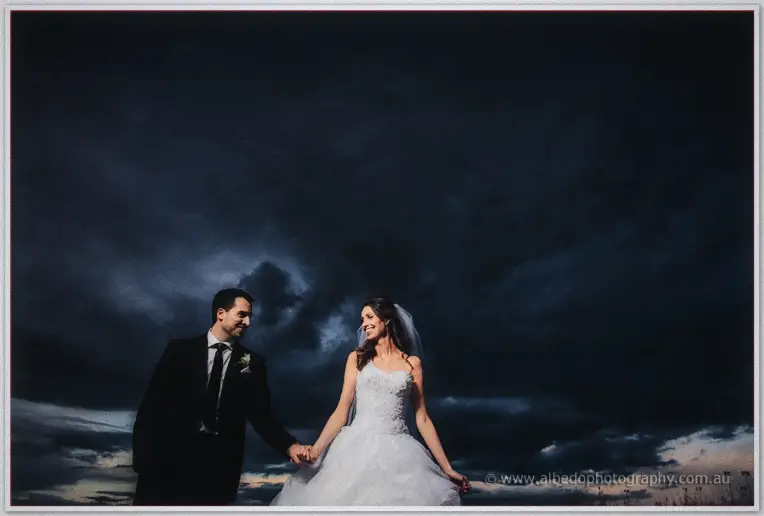 Hand in hand under brooding clouds, Michele and Nick pause in the open parkland at dusk.