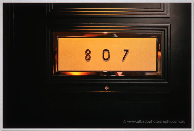 A warm-lit brass plate marks room 807 on the dark timber door of the hotel suite.