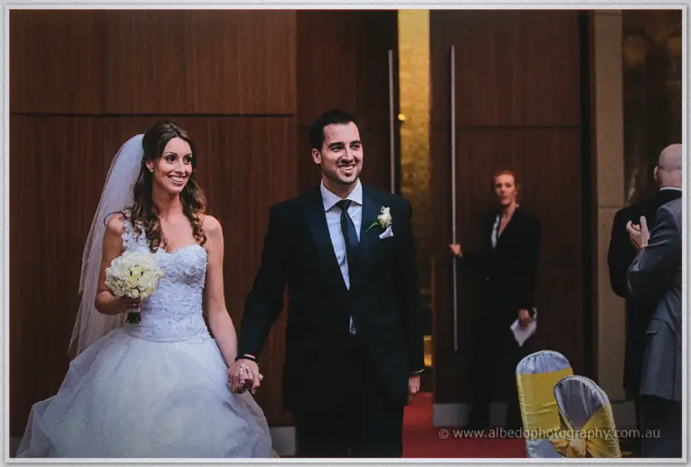 Beaming, the couple enters the Astral Ballroom to begin their reception as staff look on.