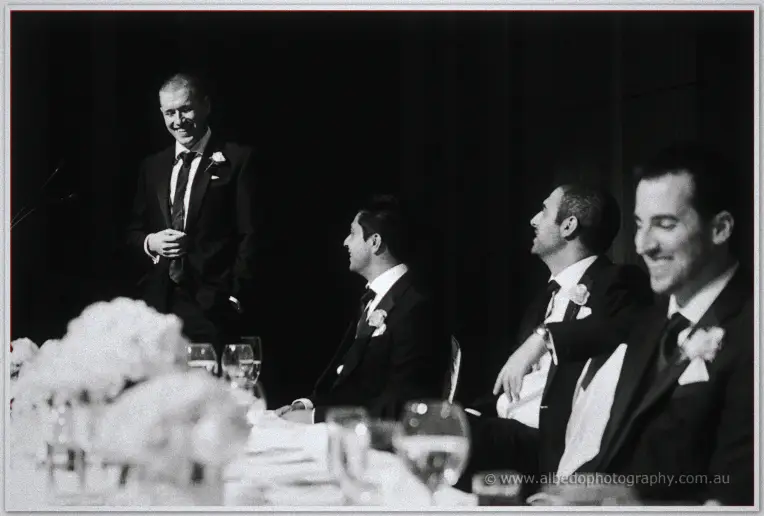 Black and white candid of the groomsmen laughing as a best man delivers his speech.
