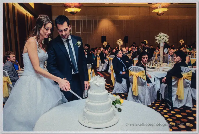 Michele and Nick cut their four-tier white cake before a full ballroom of smiling guests.