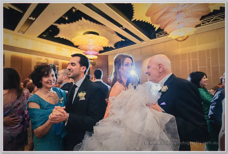Michele dances arm in arm with guests on the packed ballroom floor amid warm golden light.
