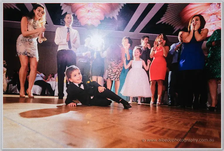 The page boy slides on his knees down the dance floor, flower girl beside him, guests delighted.