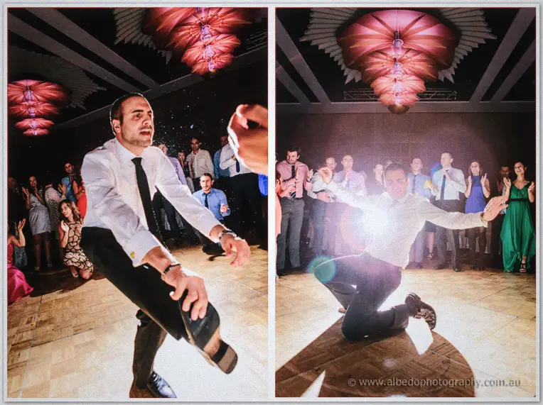 A groomsman in loosened tie kicks and knee-slides through a wild solo dance under lens flare.
