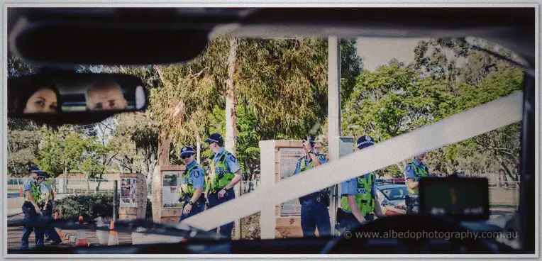Police officers gathered by the roadside seen through a car windscreen, the bride reflected in the mirror
