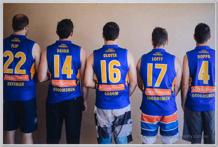 Groomsmen from behind in numbered blue football jumpers, best man and groom printed across their backs