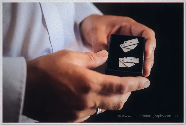 Close-up of the groom's hands holding a black gift box of playing-card cufflinks in low window light