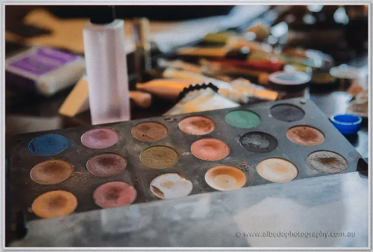 Well-used eyeshadow palette in warm bridal prep tones surrounded by scattered makeup brushes and bottles