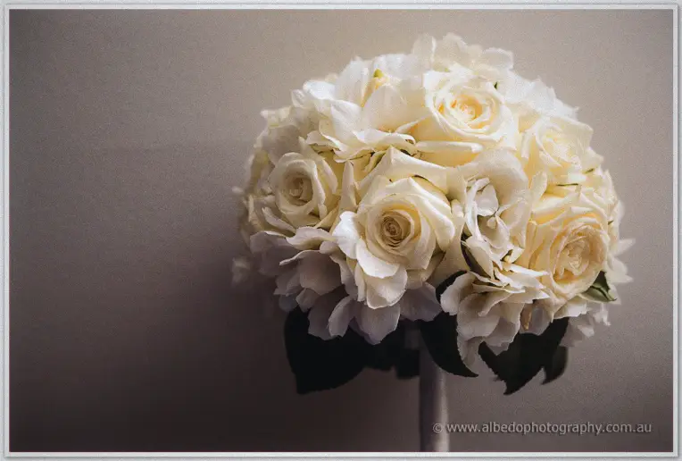 Round ivory bridal bouquet of roses and hydrangeas resting against a softly lit neutral wall