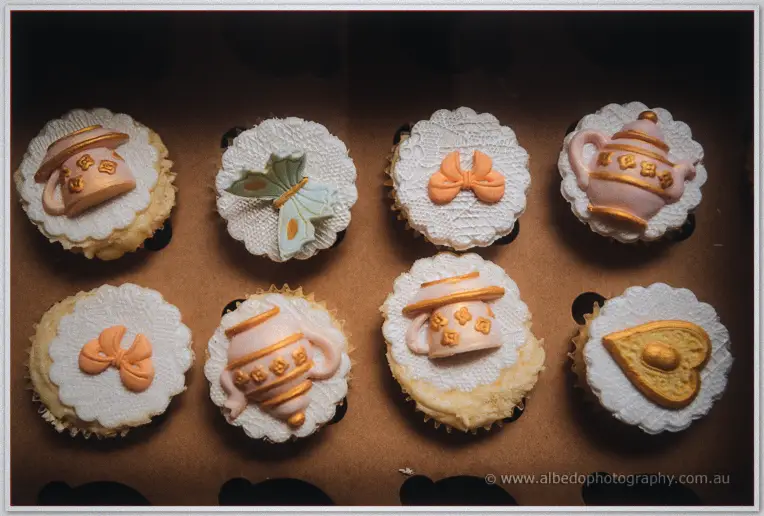 Vintage-style cupcakes topped with teapot, bow and butterfly icing in soft peach and cream tones