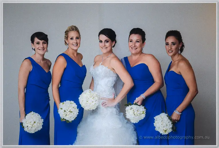 Allison with her four bridesmaids in cobalt gowns holding white hydrangea posies against a grey wall