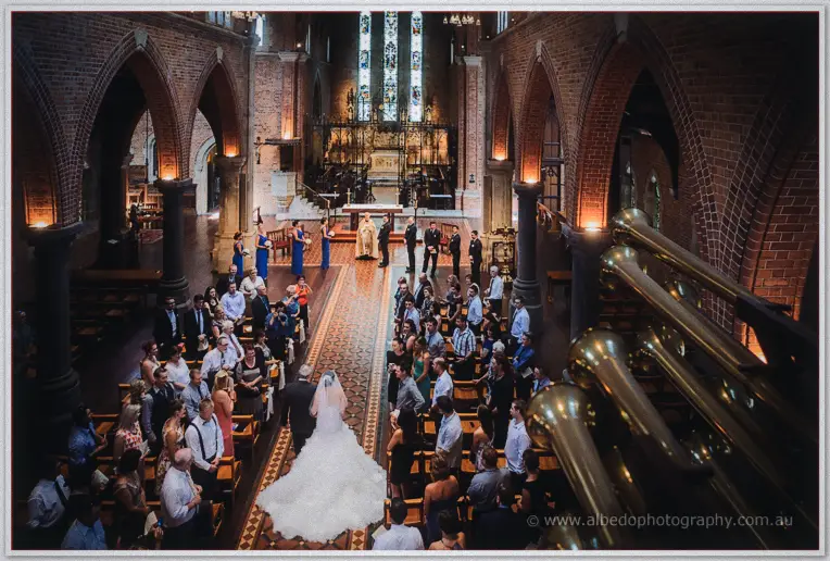 Wide view down St George's Cathedral as Allison walks the aisle past standing guests beneath stained glass