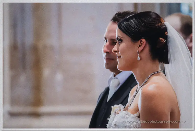 Allison smiling in profile beside Greg during the ceremony inside St George's Cathedral