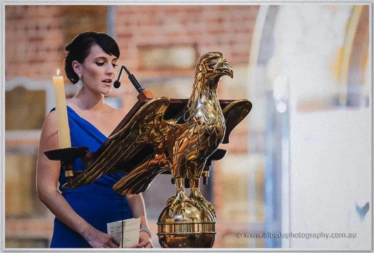 Bridesmaid in blue reading from the brass eagle lectern during the cathedral ceremony