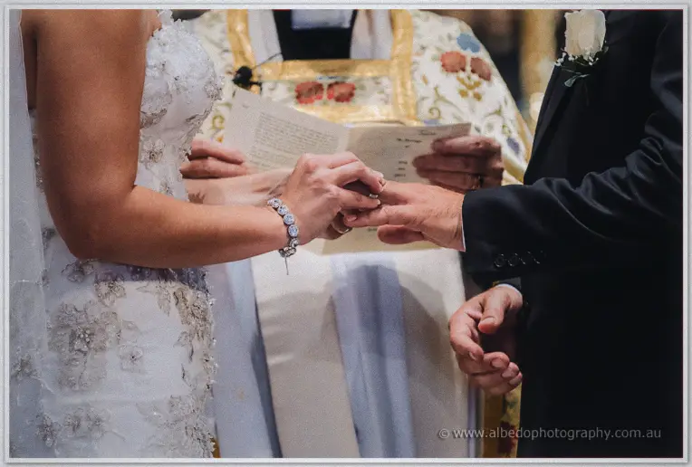 Close-up of Allison sliding the wedding ring onto Greg's finger at the cathedral altar