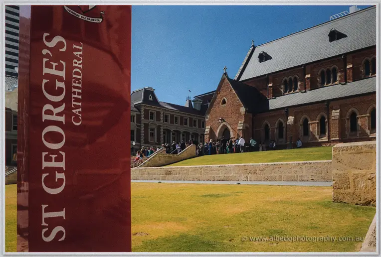 Red St George's Cathedral sign before the brick Gothic church and sunny lawn in Perth