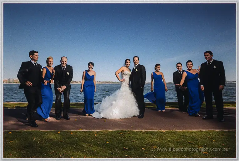 Full bridal party posing on the riverfront path with Allison and Greg laughing at the centre