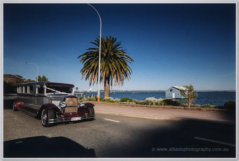 Vintage maroon and silver stretch limousine parked by the Swan River beneath a tall palm