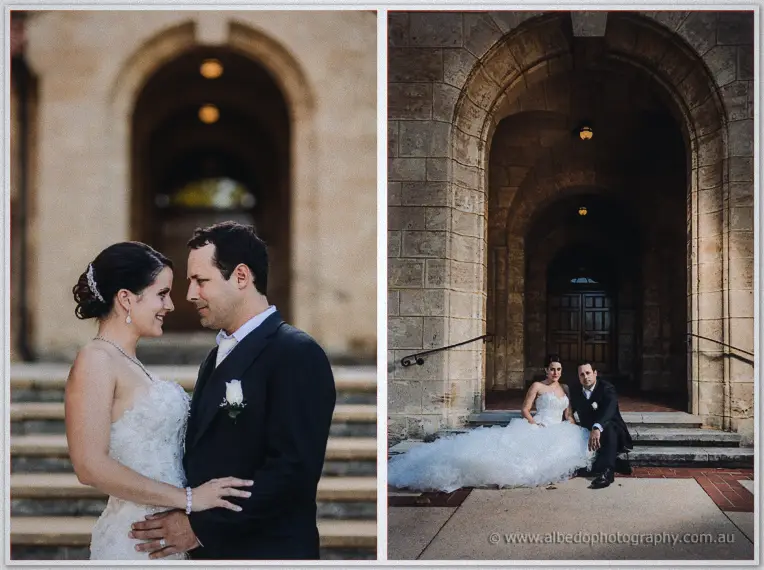 The couple seated side by side on stone steps beneath a deep arched entryway, gown pooling around them.