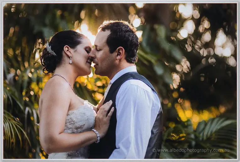 A tender nose-to-nose moment between Allison and Greg, sunset flaring through the palms behind them.
