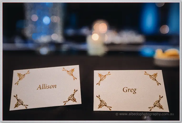 Gold-lettered place cards reading Allison and Greg glow against candle bokeh on the bridal table.