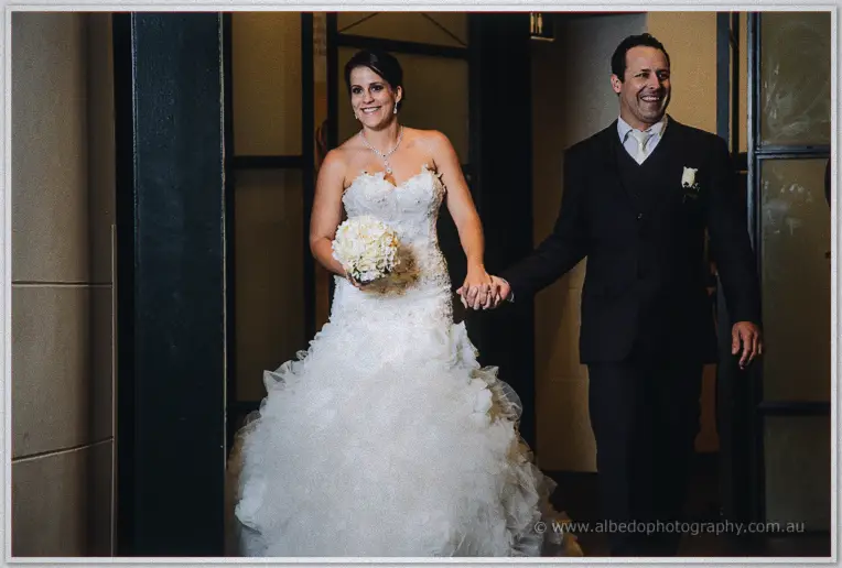 Allison and Greg make their entrance hand in hand, her ruffled gown filling the doorway as both beam.
