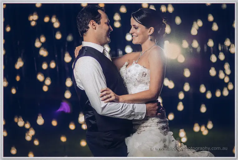 A slow dance beneath dozens of hanging festoon bulbs, Allison smiling up at Greg in the warm glow.