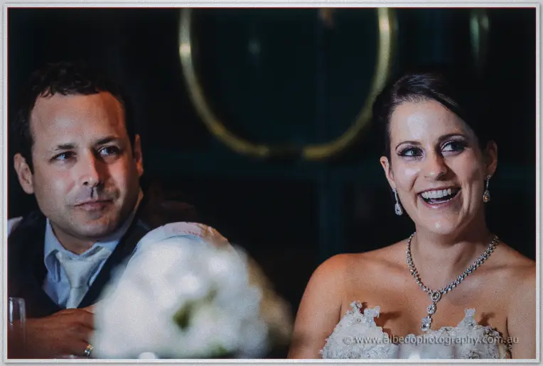 Allison roaring with laughter beside a deadpan Greg as speeches land at the dimly lit bridal table.