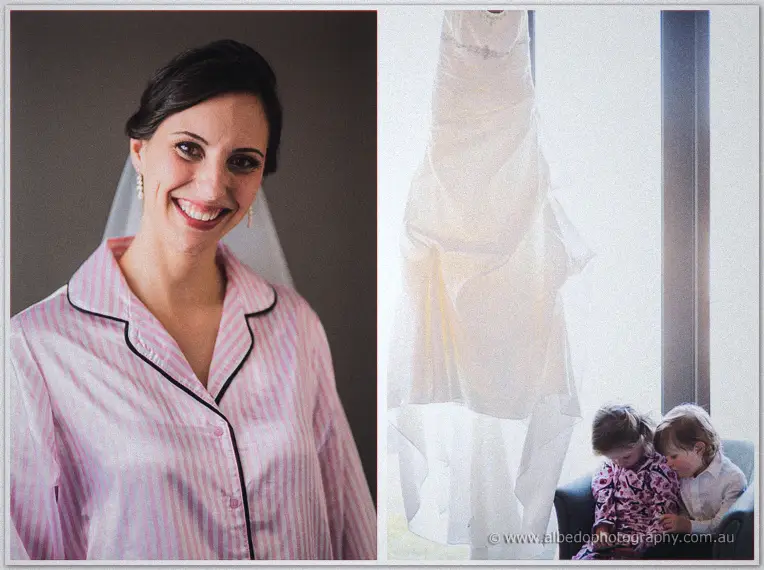 Smiling bride in pink striped pyjamas beside her ivory gown hanging in bright window light by two children