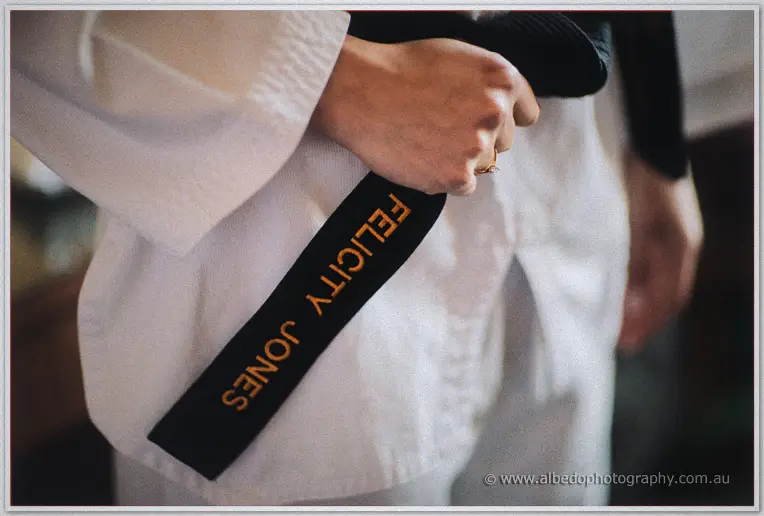 Close-up of a hand gripping a black taekwondo belt embroidered with Felicity Jones over a white uniform