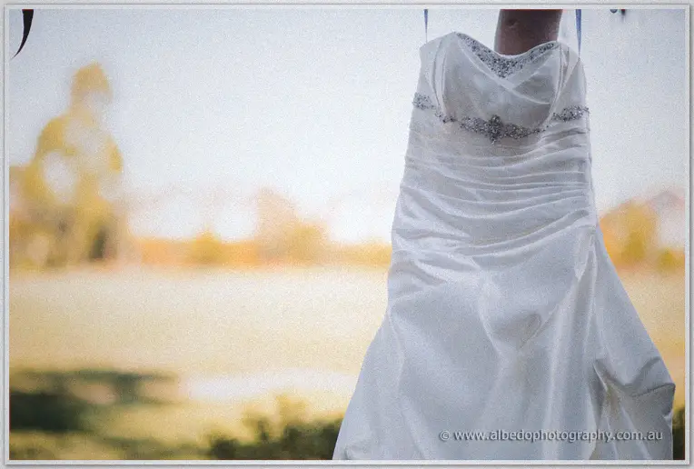 Strapless wedding gown with beaded waist hangs against a soft golden paddock backdrop at the estate