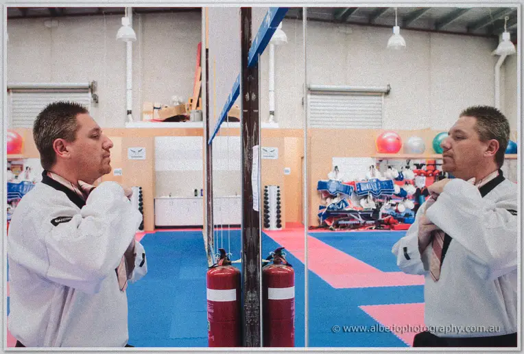 Diptych of Mark tying his tie in a white taekwondo uniform, mirrored inside a martial arts gym