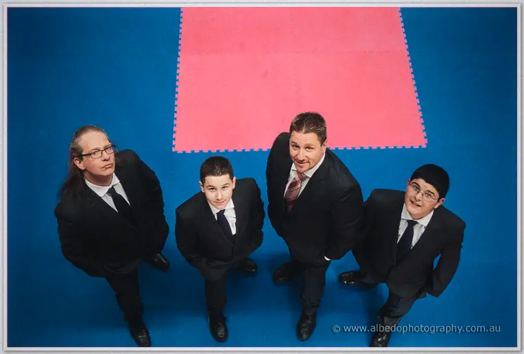 Mark and his groomsmen in dark suits gaze up against the blue mats of a martial arts dojo