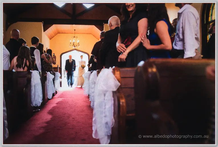 Felicity walks the red-carpeted chapel aisle on her father's arm as guests turn and watch
