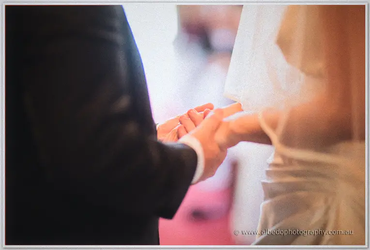 Close-up of Mark gently holding Felicity's hand at the altar, veil and suit in soft focus