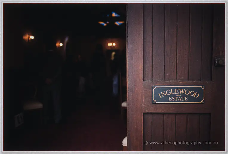 Aged timber door with an Inglewood Estate plaque opens into a dim, lamplit chapel