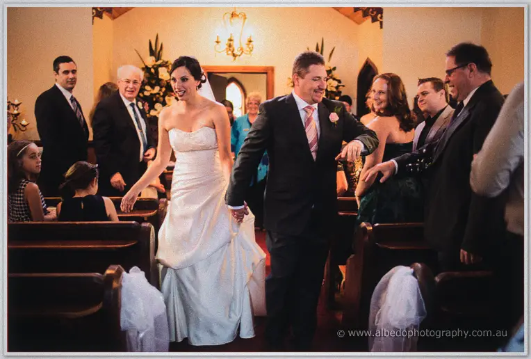 Felicity and Mark walk hand in hand up the aisle as guests clap and smile around them