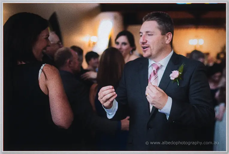 Mark gestures mid-conversation at the lively reception, guests mingling in warm evening light