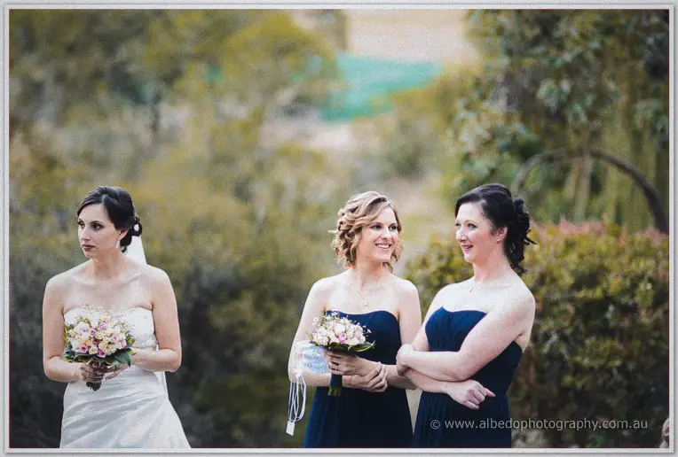 Felicity and her bridesmaids in navy dresses hold pastel bouquets amid soft green bushland.