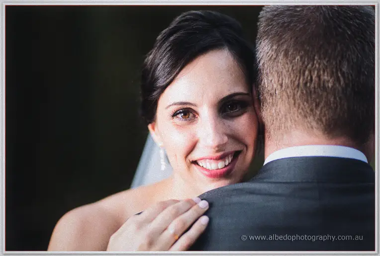 Felicity beams over Mark's shoulder in a tight embrace, soft light on her face.