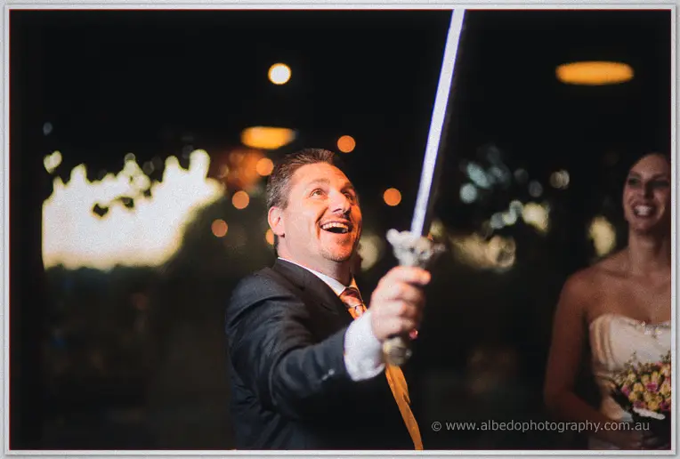Mark brandishes a glowing toy sword under festoon lights, Felicity laughing behind.